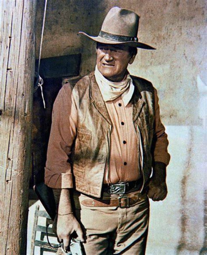 John Wayne holding a hand up waving wearing a suit and hat